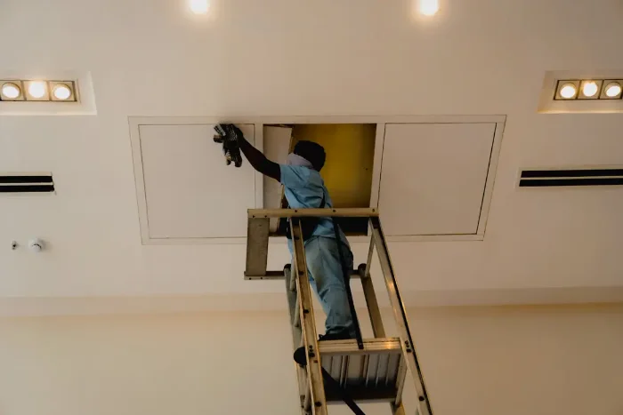 Técnico en escalera junto a un panel de acceso del techo