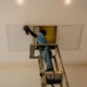 Técnico en escalera junto a un panel de acceso del techo