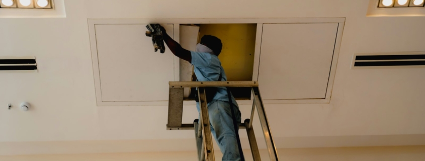 Técnico en escalera junto a un panel de acceso del techo